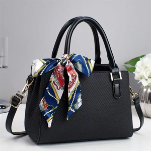 Detail of black textured handbag with golden hardware and vibrant floral scarf accessory