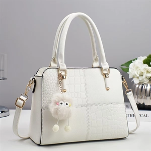 Detalle de bolso blanco con relieve de cocodrilo, herrajes dorados y adorno de felpa