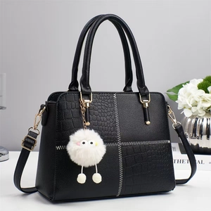 Detalle de bolso negro patchwork con textura de cocodrilo y colgante de peluche