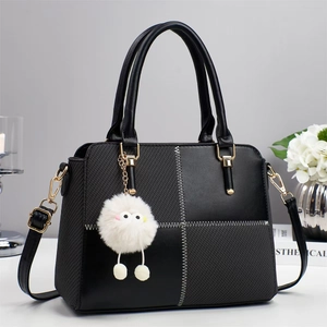Detail of black crossbody bag featuring contrast stitching, gold buckle, and plush charm