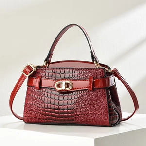 Chic burgundy crocodile pattern handbag with gold clasp on white geometric pedestal
