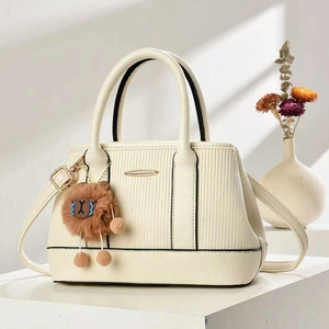 Detail of cream white textured leather handbag with plush charm on a geometric stand