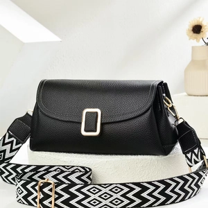 Black pebble leather crossbody bag with wide geometric strap on a stone pedestal