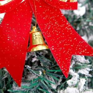 Red flocked Christmas bow with gold bell and glitter on a snowy Christmas tree branch