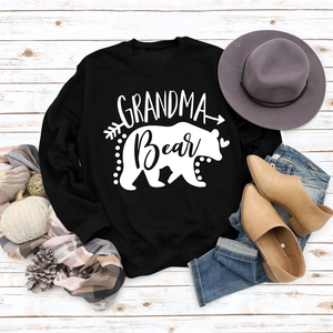 Flat lay of Grandma Bear sweatshirt with autumn decor, hat, jeans, and scarf on wood
