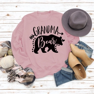 Detailed flat lay of pink Grandma Bear sweatshirt with black graphic print and autumn decor