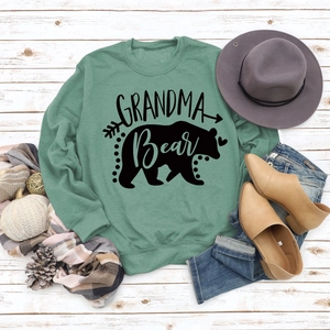 Flat lay of green Grandma Bear sweatshirt with autumn decor on white wood background
