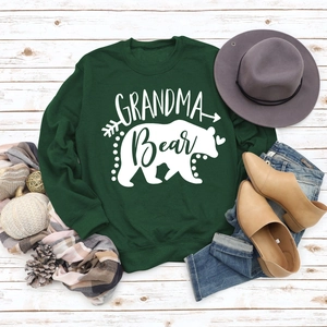 Close-up of Grandma Bear print on dark green sweatshirt with autumn props on wood