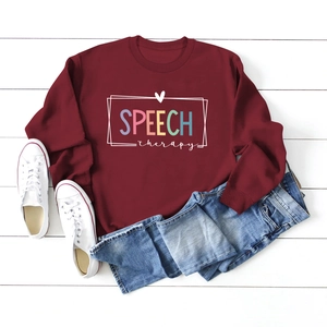 Flat lay of maroon long-sleeve sweatshirt with colorful speech therapy lettering and jeans