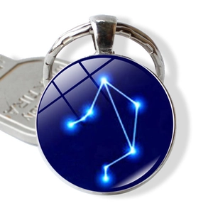 Macro detail of Libra constellation glass dome pendant and metal keyring on white background