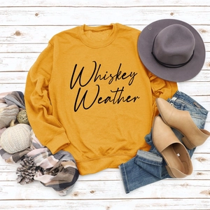 Flat lay of mustard yellow sweatshirt with Whiskey Weather lettering and autumn accessories