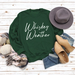 Flat lay of dark green sweatshirt with Whiskey Weather print and autumn accessories