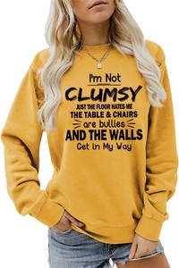 Detailed shot of ginger yellow crewneck sweatshirt featuring black I'm Not Clumsy slogan