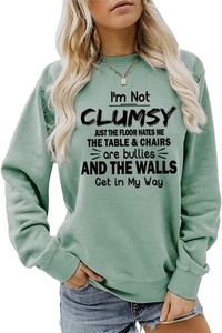 Detail of mint green sweatshirt featuring black I'M NOT CLUMSY typography and ribbed neckline