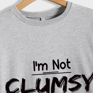 Grey crew neck sweatshirt featuring I'M NOT CLUMSY slogan print on wooden hanger
