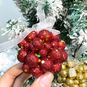 Red glitter foam Christmas ball ornaments held by hand against a festive tree background