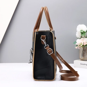 Side view of black faux leather tote with brown trim and silver chain detailing