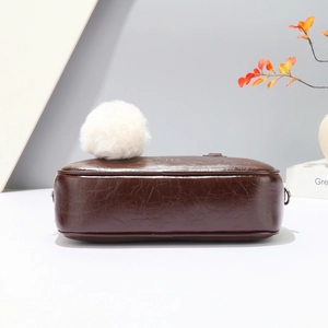 Close-up of dark brown leather Boston bag with a large white plush ball charm detail