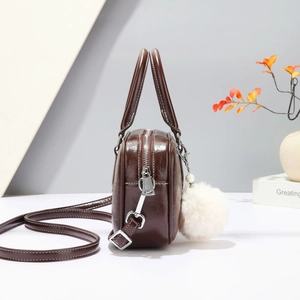 Detail view of dark brown Boston bag with oil wax texture and fluffy pompom charm