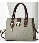 Close-up of crocodile textured gray leather bag with dark brown handles and golden lock