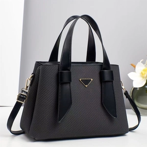 Detail of grey fabric tote with leather trim and golden triangular metal emblem