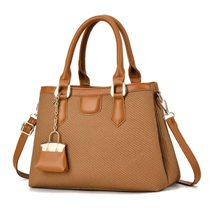 Close-up of woven fabric handbag with brown faux leather trim and mini bag charm