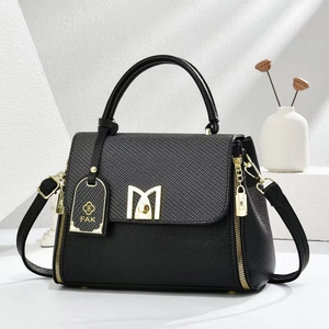 Detail of black pebbled leather crossbody bag with M-shaped gold hardware lock and tag