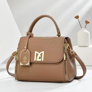 Detail of tan leather crossbody bag with fabric flap and golden M-shaped buckle