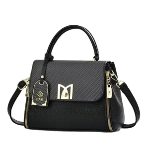 Black leather crossbody bag with gold M-buckle and textured finish on white background