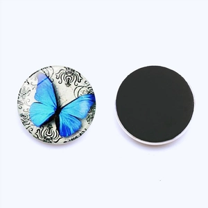 Detail view of round glass fridge magnet with blue butterfly pattern and magnetic back