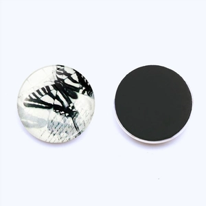 Macro view of 25mm round glass magnet showing monochrome butterfly art and magnetic back