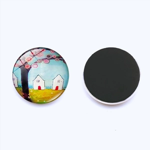 Detail view of round glass magnet featuring colorful artistic house and tree illustration