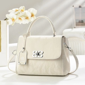 Detail of cream pleated leather bag with a silver floral metal lock and orchid accent