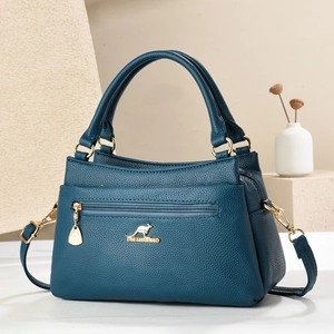 Detail der petrolblauen Handtasche aus Narbenleder mit goldenem Logo und Schultergurt