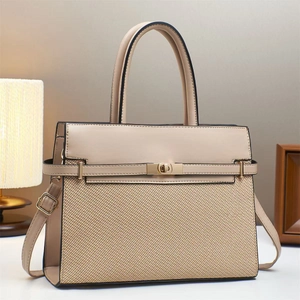 Detail of beige textured handbag with gold twist lock and leather stitching on white desk
