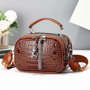 Close-up of brown crocodile texture bag with double zippers and silver bear pendant