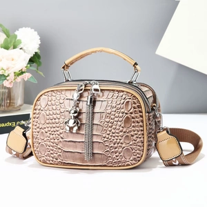 Close-up of khaki faux crocodile texture bag with bear pendant and tassel details