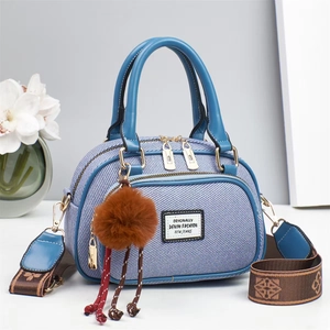 Blue denim crossbody handbag with leather handle and decorative brown plush ball charm