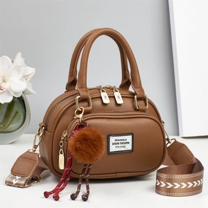 Nahaufnahme der braunen Handtasche mit gewebtem Schultergurt und Plüsch-Anhänger