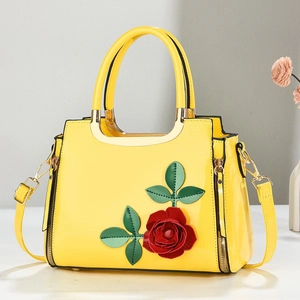 Detail of yellow patent leather handbag with red 3D rose flower and gold metal hardware