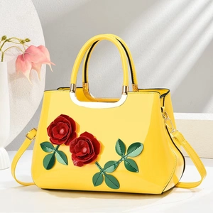 Close-up of yellow patent leather handbag with 3D red roses and gold hardware details