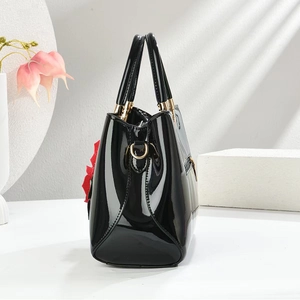 Detail of glossy black patent leather handbag featuring a red floral charm and gold hardware
