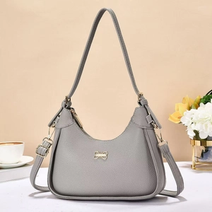 Grey vintage half-moon shoulder bag with golden bow detail on a minimalist table