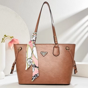 Close-up of brown faux leather tote bag with silk scarf handle and metal logo detail