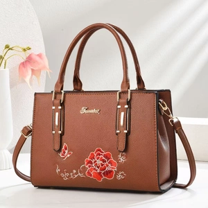 Detailaufnahme der braunen Lederhandtasche mit roter Blumenstickerei und metallischem Logo-Schild