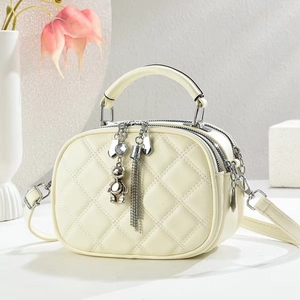 Petit sac bandoulière matelassé crème avec breloque ours et poignée sur fond minimaliste