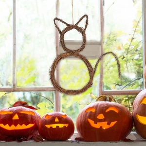 Detail of cat-shaped wicker wreath hanging by glowing pumpkins for Halloween decor