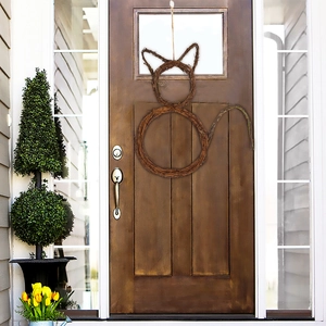 Detailed view of a handmade cat-shaped rattan wreath hanging on a solid wood front door