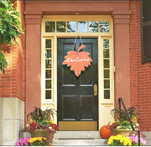 Close-up of orange wooden maple leaf welcome sign hanging on a rustic front door entrance
