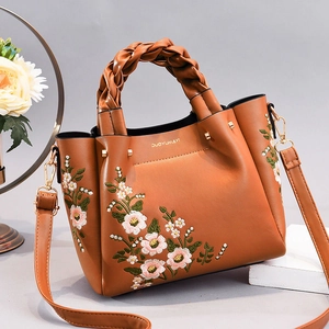 Detail of warm brown leather handbag with pink floral embroidery and woven top handle